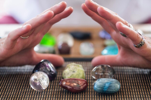 Photo close-up of human hand over multi colored gemstone on table