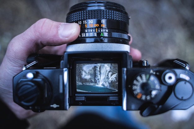 Close-up of human hand photographing waterfall with digital camera