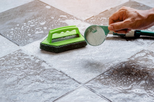 Photo close up a human hand pours detergent onto the wet tile floor to clean it.