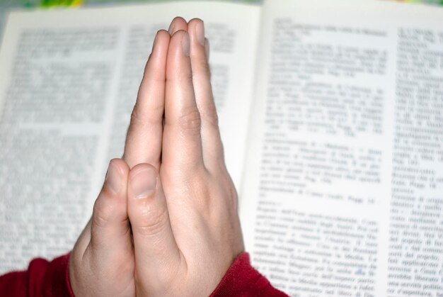 Photo close-up of human hand praying against book