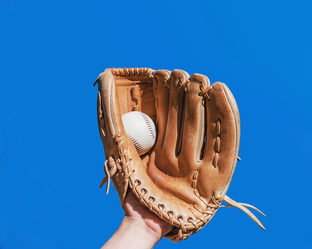 Foto close-up di una mano umana che indossa un guanto che tiene la palla mentre gioca a baseball contro un cielo blu limpido