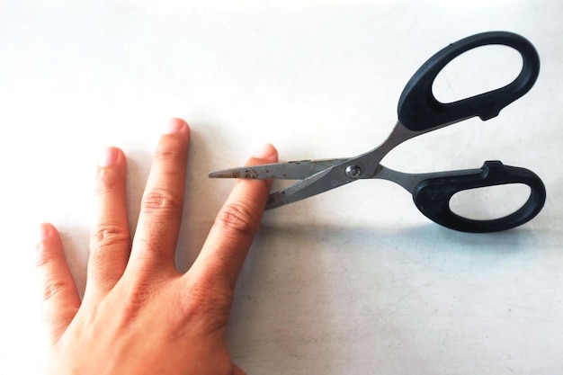 Photo close-up of human hand with scissors on white table