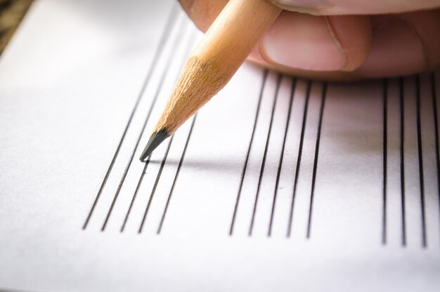 Photo close-up of human hand writing with pencil on lined paper