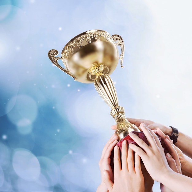 Close-up human hands holding golden Trophy on blue sky background