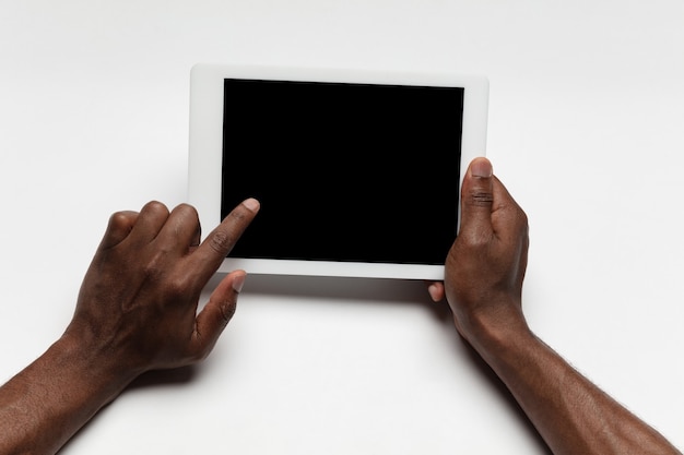 Close up of human hands using tablet isolated on white background. Top view. Copyspace, blank screen. Surfing, online shopping, scrolling, betting, working. Education and business concept.