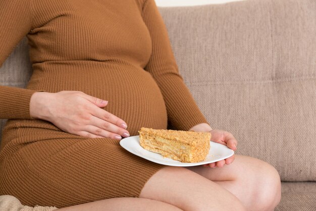 Close up of hungry pregnant woman is eating a piece of tasty cake relaxing on the sofa at home Sweet cravings during pregnancy