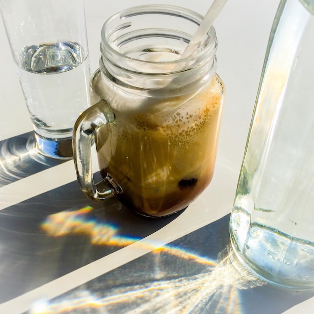 Photo close-up of iced coffee in mug and drinking water served on table