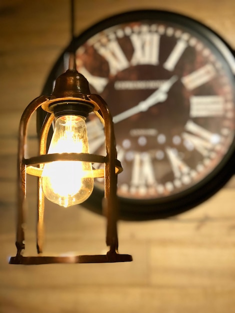 Photo close-up of illuminated light bulb against wall clock