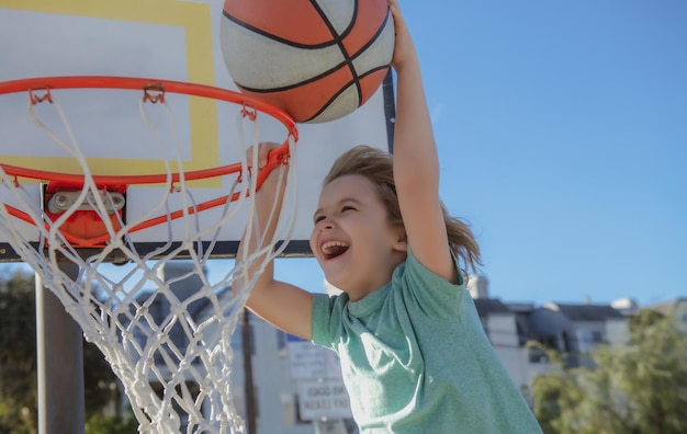 バスケットボールの興奮した子供プレーヤーが遊び場の子供スコアリングで屋外でボールをダンクする画像をクローズアップ