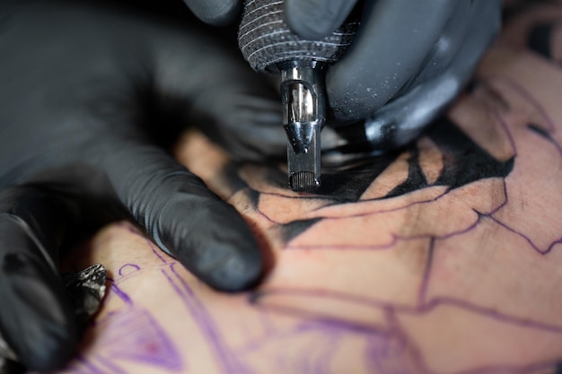 Close up image of the bearded tattoo male artist makes a tattoo on a female leg