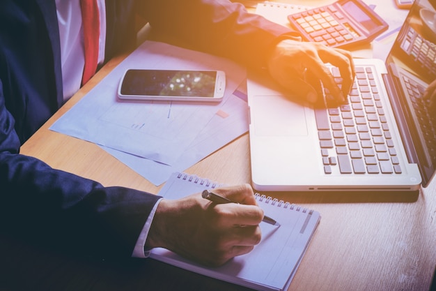 Close up image of business man in shirt suit drink coffee and check time on cellphone. Male freelancer sending e-mail after work on laptop computer