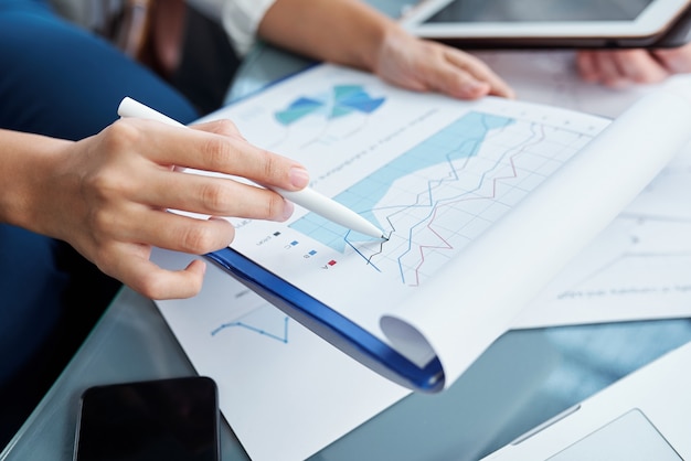 Close-up image of businesswoman pointing at financial chart and analyzing sales and expenses