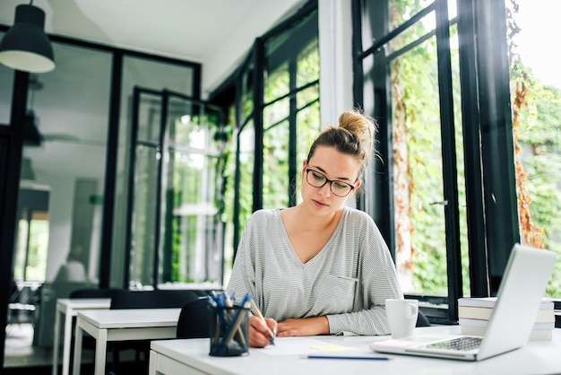 Close-up image of casual young woman writing essay at desk.