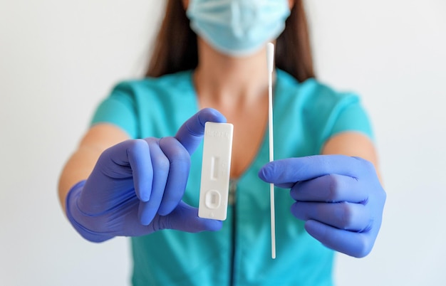 Close-up image of doctor holding covid rapid antigen test and swab.