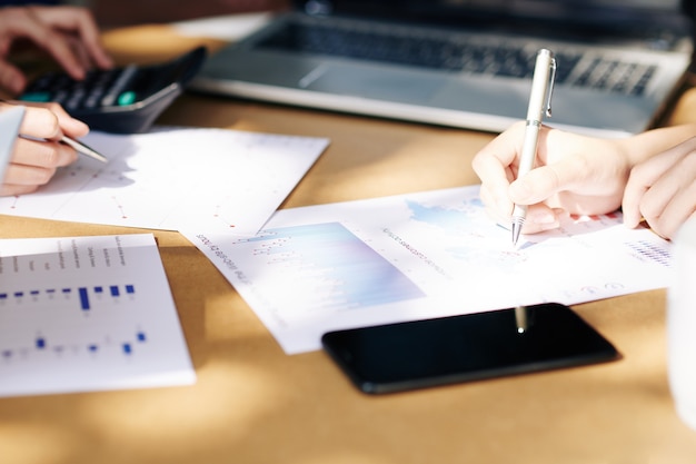 Close-up image of entrepreneurs working with chats and reports at office table