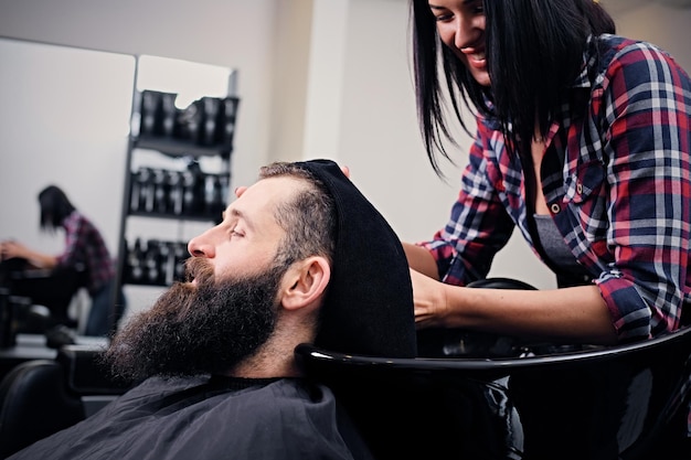 Close up image of female hairdresser washing bearded men's hair before haircut in a saloon.