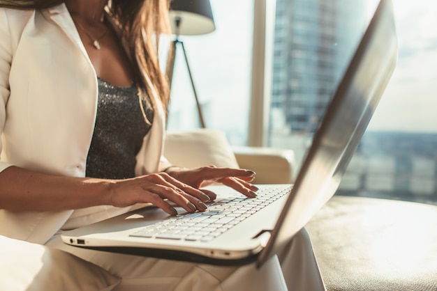 Close-up image of female hands typing on laptop keyboard in modern office.