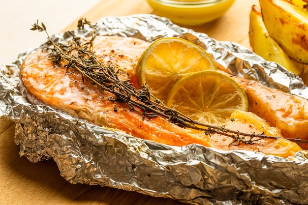 Close up image of the fish baked in foil with branch of thyme and two slices of lime on it. Potatoes 