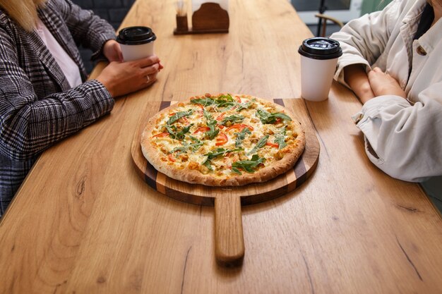 Photo close-up image of friends sharing traditional italian pizza and drinking tea in a cafe