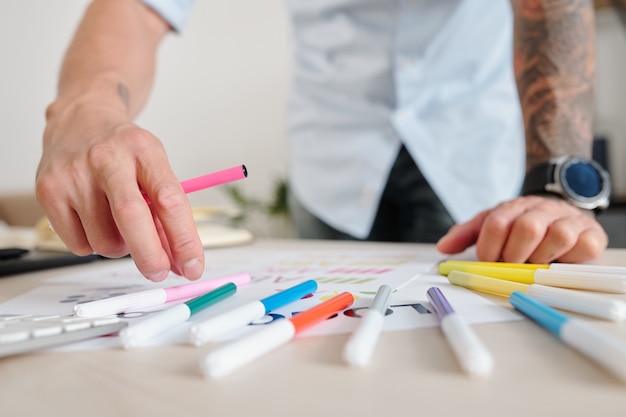 Photo close-up image of graphic designer using felt tip pens of various color when coloring logo mockup