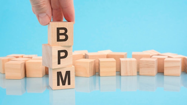 Close up image hand of a man holding a wooden cube with letters BPM on wooden cubes blue background with copy space