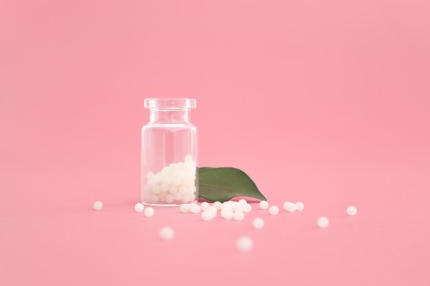 Close-up image of homeopathic globules in glass bottle on pastel pink background. Homeopathy pharmacy, herbal, natural medicine, alternative homeopathy medicine, healthcare. Free space, copy space.