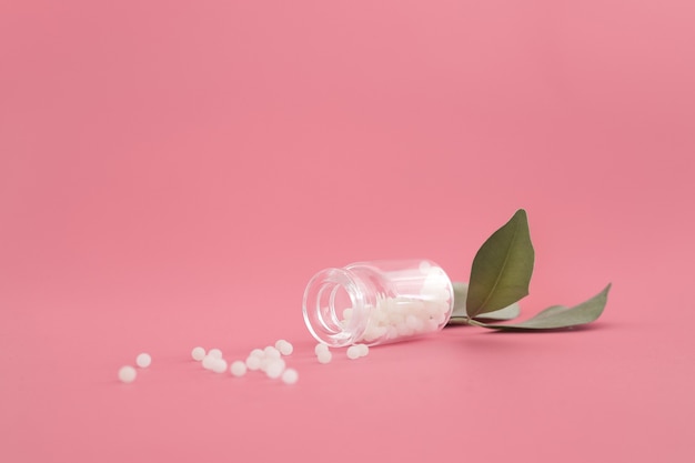 Close-up image of homeopathic globules in glass bottle on pastel pink background. Homeopathy pharmacy, herbal, natural medicine, alternative homeopathy medicine, healthcare. Free space, copy space.