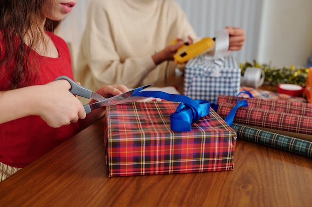 Изображение крупным планом маленькой девочки, перерезающей ленточку, когда она упаковывает рождественские подарки со своими друзьями