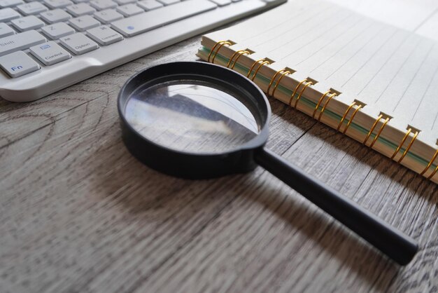 Close up image of magnifying glass notebook and computer keyboard on table Research study and investigate concept