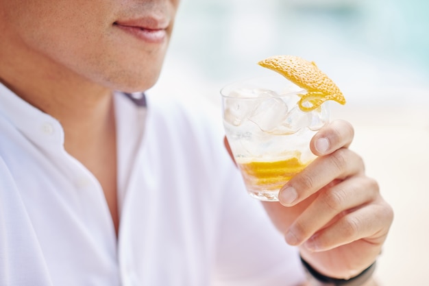 Foto immagine del primo piano dell'uomo che tiene un bicchiere di gin tonic con buccia d'arancia