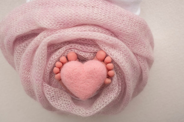 Close-up image of newborn baby's feet on a pink blanket. Pink knitted woolen heart in the toes of a newborn baby.