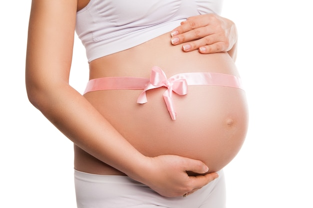 白の上のピンクのリボンで妊娠中の女性のおなかの画像をクローズアップ