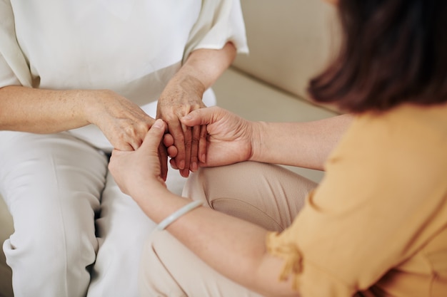 Close-up image of senior woman holding hands of her friend when trying to reassure her