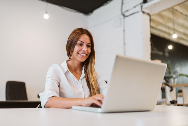 Close-up image of smiling young woman using laptop in bright creative studio.