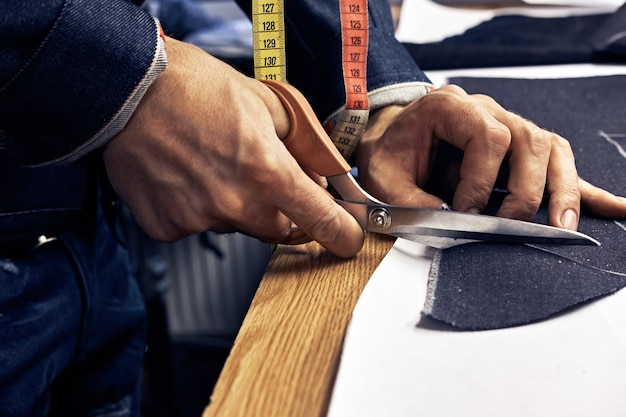 Close-up image of a tailor cutting dark cloth at a sewing workshop.