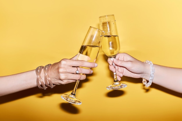 Close up image of two people clinking champagne glasses on yellow background