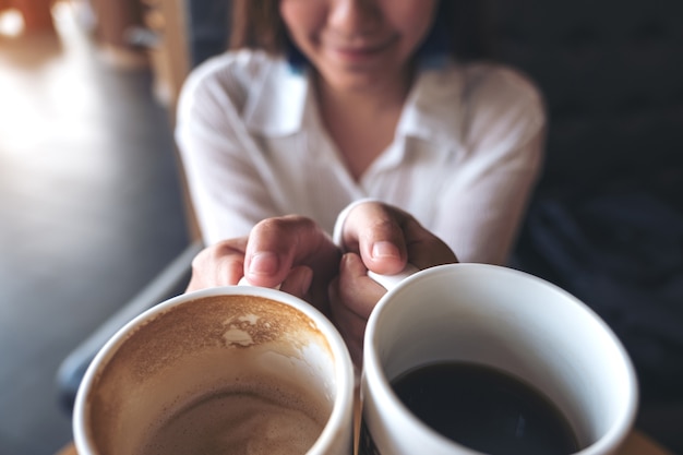 Close up image of a woman holding two white coffee mugs in cafe