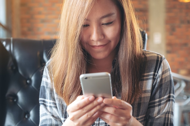 Chiuda sull'immagine di una tenuta della donna, usando e guardando lo smartphone in caffè