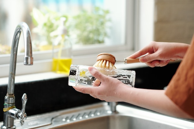 台所の流し台で皿洗いをするときに環境にやさしいブラシを使用している女性のクローズアップ画像