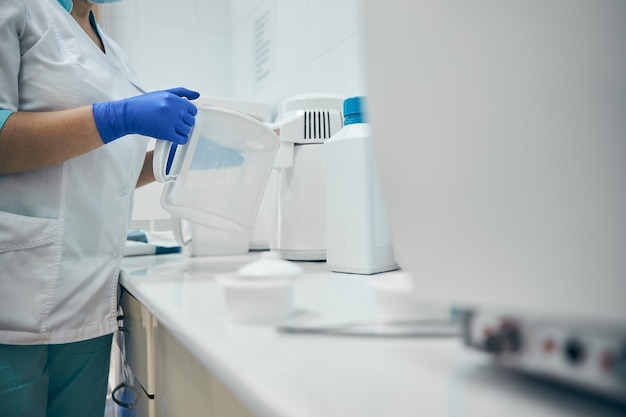 Immagine ravvicinata di una donna che lavora alla scrivania del dentista con una preparazione disinfettante in un contenitore nello studio dentistico