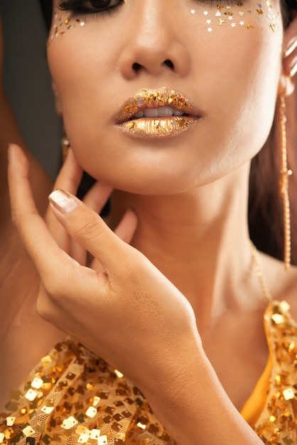 Close-up image of young woman with full lips with golden lipstick and golden gliter stars as a part of Hallooween makeup