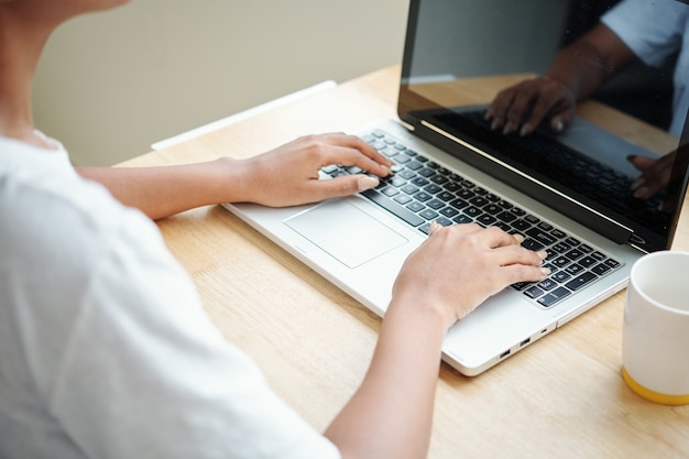 Close-up image of young woman working on laptop, programming or answering e-mails