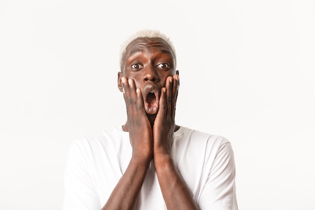 Close-up of impressed and amazed handsome african-american blond man, drop jaw and saying wow astonished, holding hands on face