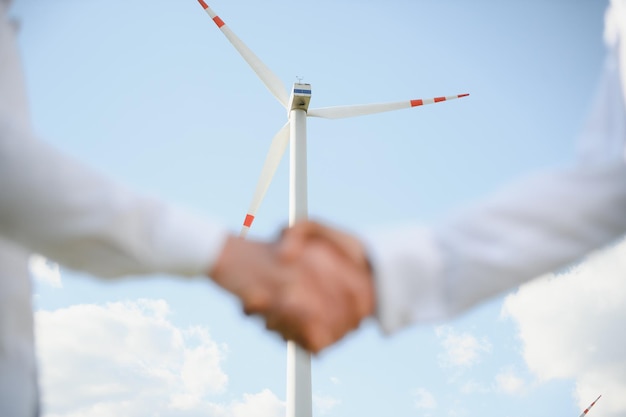 Close up of indian technician and inspector shaking hands while standing on farm with wind turbines Concept of people teamwork and eco friendly energy