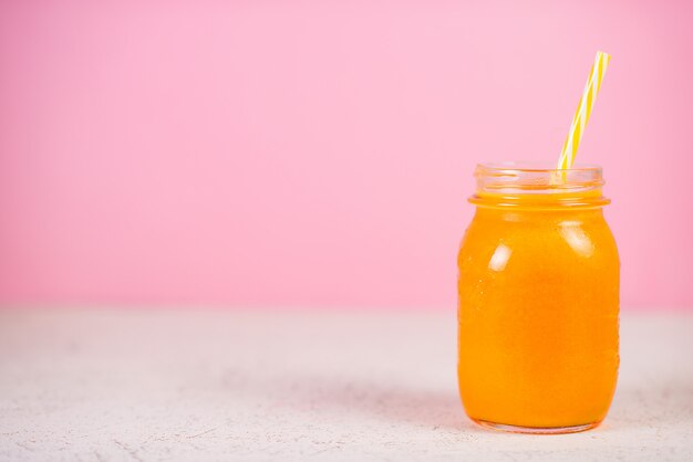 Close up is een potje verse gele smoothie gemaakt van natuurlijk fruit op een roze achtergrond.