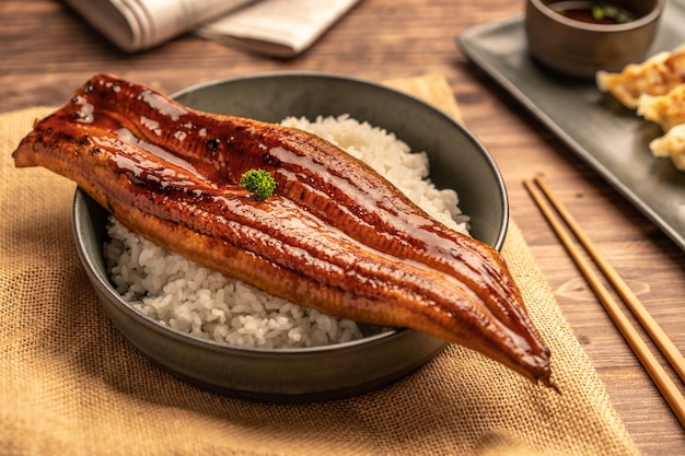 クローズアップの日本の焼きうなぎをご飯の上にのせたり、うなぎ丼を皿に盛り付けたりします。レストランのテーブルで日本食