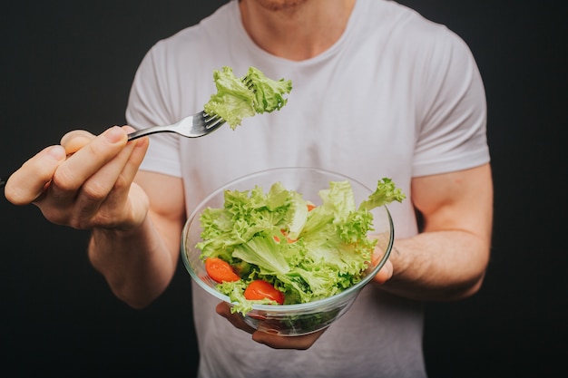 Close-up jonge blonde man in wit t-shirt houdt plaat van salade