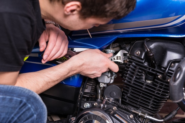 Close-up jonge man bezig met sommige delen van zijn blauwe motor met behulp van een moersleutel handgereedschap