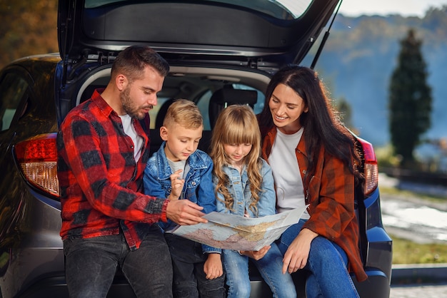 Крупным планом радостной приятной семьи, которая собирается в отпуск с детьми-подростками и использует дорожную карту, чтобы выбрать правильный путь на автомобиле
