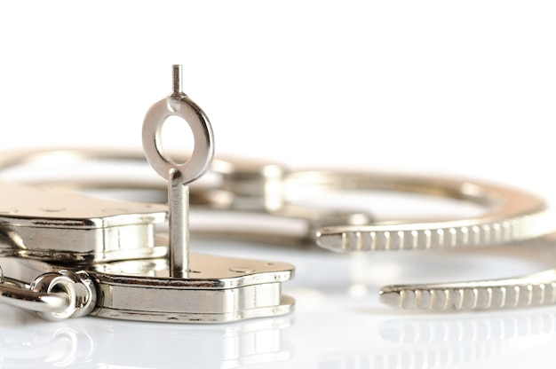 Close-up of a key opens a handcuff lying on a white table. Concept Release from imprisonment. Freedom from stereotypes and complexes. Advertising space